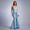 Woman wearing a floor-length ice blue strapless satin gown with a large side ruffle detail and mermaid flare on a light gray background