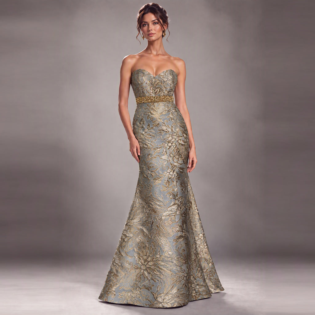 A strapless sweetheart mermaid gown in shimmering metallic gold and silver jacquard fabric, featuring a gold beaded waistband, modeled against a neutral gray studio background.
