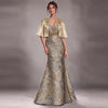 A woman models a formal evening gown with a matching short satin cape. The dress features a strapless bodice with a V-neckline, a gold beaded waistband, and a floor-length mermaid silhouette.