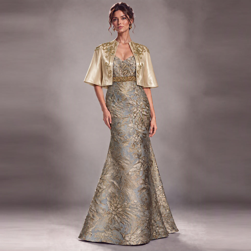 A woman models a formal evening gown with a matching short satin cape. The dress features a strapless bodice with a V-neckline, a gold beaded waistband, and a floor-length mermaid silhouette.