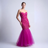 A woman wearing a bright fuchsia pink strapless mermaid gown with a heavily beaded bodice and a voluminous floor-length tulle skirt, standing against a neutral studio background.