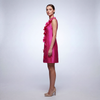 Profile view of a sleeveless fuchsia mini dress showing the structured A-line sheath fit and dimensional floral appliqués paired with nude heels.