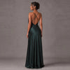 A woman modeling a floor-length dark green satin gown from the back, showing a crisscross open back and a full skirt, against a textured gray studio backdrop.