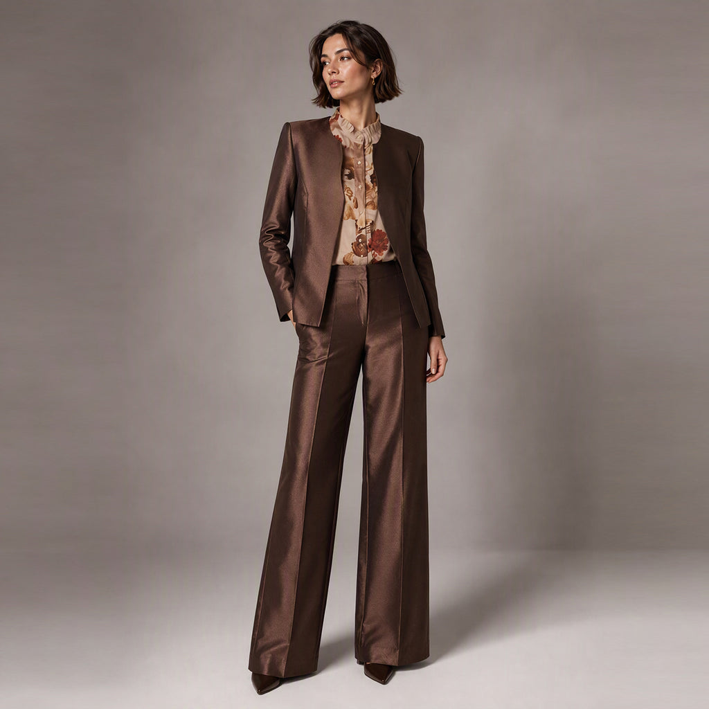 A woman modeling a brown Silk wool two-piece suit with a matching blazer and wide-leg trousers, layered over a beige floral print blouse, against a neutral gray studio background.